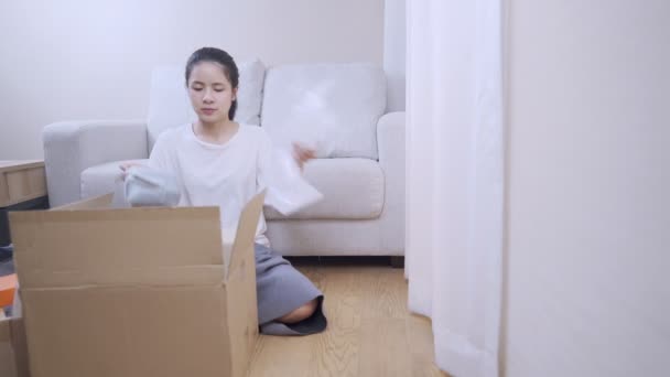 shot of young putting things into the parcel carton box, preparing to move out, sit down couch on the background, Multitasking works house arranging, budget Relocating financial crisis, stay at home - Footage, Video