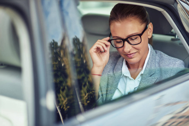 Belle femme d'affaires d'âge moyen ajustant ses lunettes tout en étant assis sur le siège arrière en taxi - Photo, image