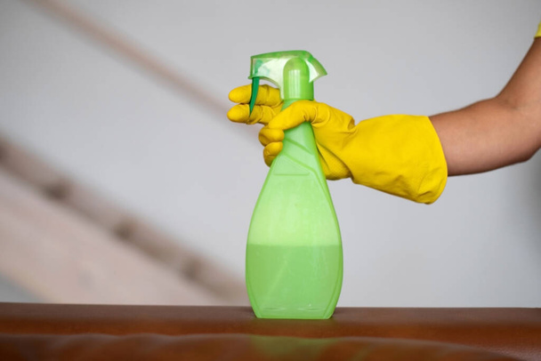 Уборка, уборка. Гигиена и чистота на кухне. Девушка надевает жёлтую резиновую перчатку. Рука держит зеленый баллончик - Фото, изображение