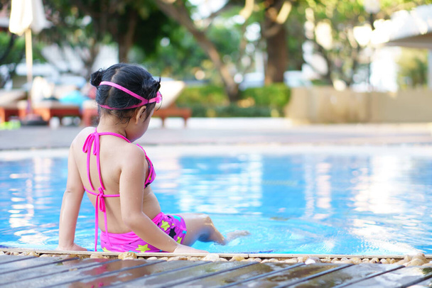 Los niños asiáticos linda o niña usan gafas y bikini se sientan con agua de juego en la piscina con diversión feliz en el parque acuático para refrescarse y relajarse con ejercicio en los viajes de vacaciones de verano en el hotel - Foto, Imagen