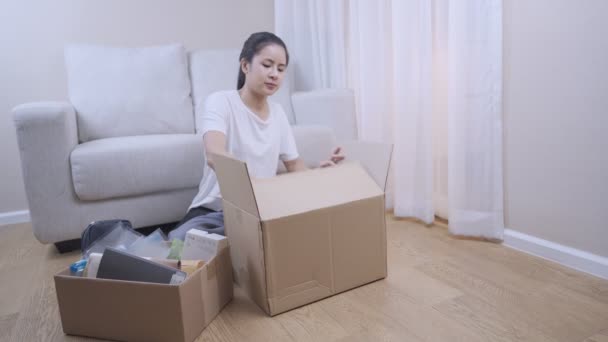 wide shot female buying new apartment, take stuff out of the parcel Storage box to arrange things, sit down couch behind, Multitasking works shore, Relocating moving in concept, stay at home - Footage, Video
