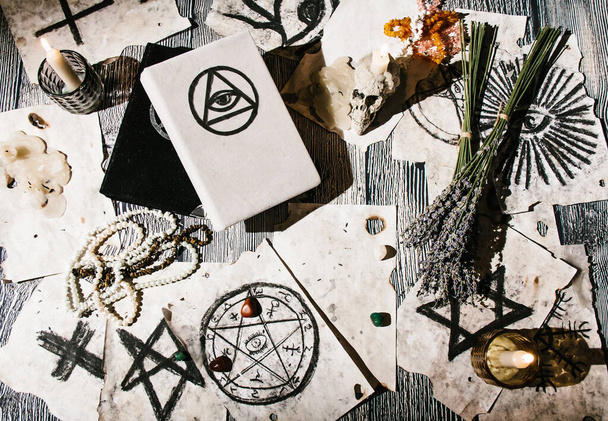 Biała księga magii leżąca na stole ze starymi rękopisami z okultystycznymi symbolami, świecami, lawendą. Pojęcie wróżby - Zdjęcie, obraz