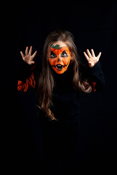 girl with pumpkin makeup scares and pretends to be a monster on a black background, Halloween celebration, low key - Φωτογραφία, εικόνα