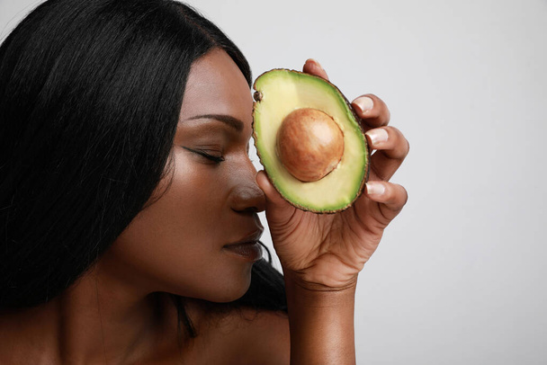 Close-up portrait of afro young woman with avocado, healthy lifestyle. Posing over white background. - Valokuva, kuva
