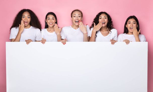 Señoras multiétnicas emocionadas sosteniendo cartel con espacio de copia, fondo rosa - Foto, imagen