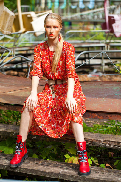 Full body portrait of a stylish model in long red flowers dress posing against the backdrop of amusement park  - 写真・画像