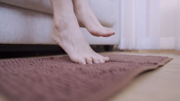 Gros plan vue de côté jeune femme peau claire pieds nus descendre du canapé au tapis de sol brun à l'intérieur de la maison salon, partie inférieure du corps, propreté de la maison, Design d'intérieur plancher stratifié en bois  - Séquence, vidéo