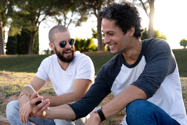 Δύο φίλοι διασκεδάζουν με το κινητό στο πάρκο το ηλιοβασίλεμα - Φωτογραφία, εικόνα