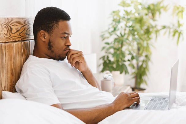 Noir gars à l'aide d'ordinateur portable de travail couché dans le lit à la maison - Photo, image