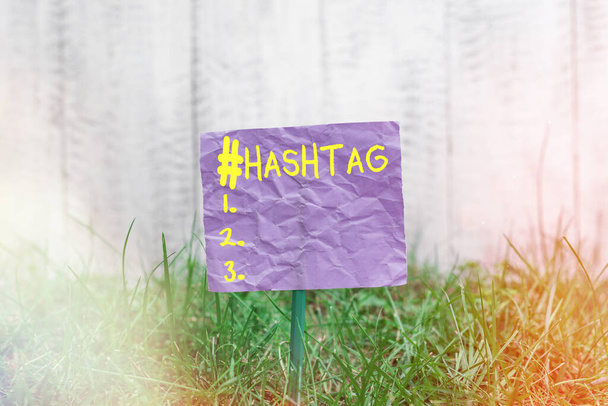 Hashtagハッシュタグを示す概念的な手書き。ソーシャルメディアのウェブサイト上のハッシュサインのハッシュタグが先行ビジネスフォトテキスト単語棒に接続され、草原の土地に配置された平野紙. - 写真・画像
