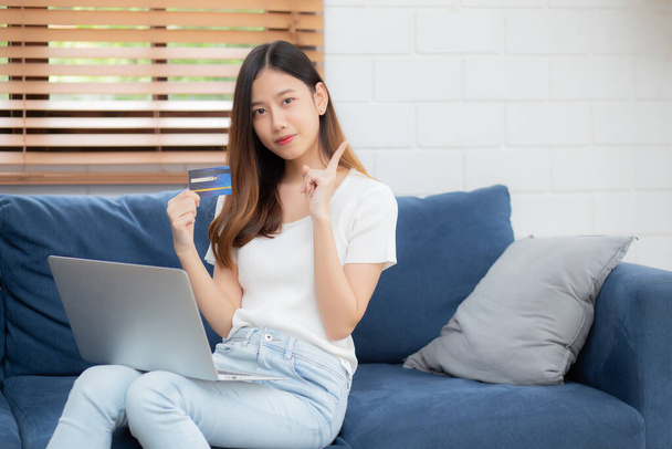 Молода азіатська жінка сидить думати ідею, використовуючи кредитну картку з ноутбуком на дивані, дівчина купує онлайн для покупки та оплати з ноутбуком на дивані, фінансами та дебетом, концепція способу життя
. - Фото, зображення
