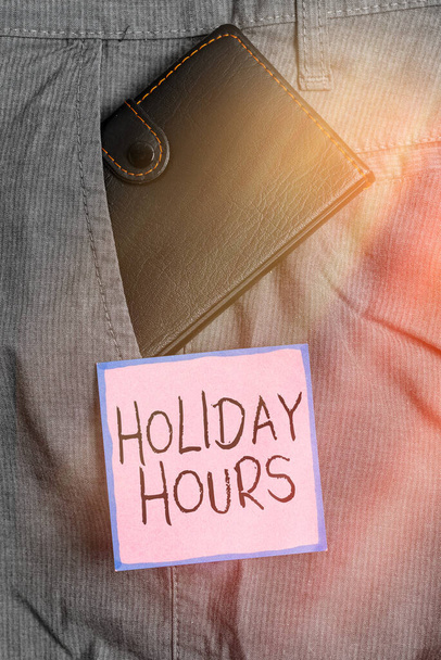 Handwriting text writing Holiday Hours. Concept meaning employee receives twice their normal pay for all hours Small little wallet inside man trousers front pocket near notation paper. - Photo, Image