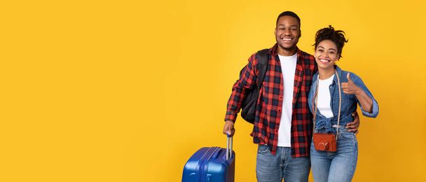 Schwarzes Touristenpaar mit Gepäck gestikuliert Daumen hoch über gelbem Hintergrund - Foto, Bild