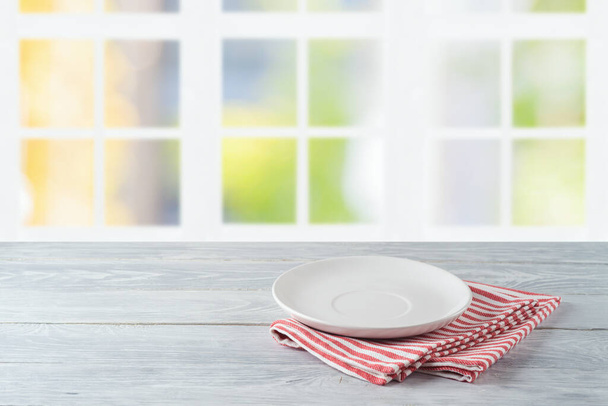 Empty plate with striped tablecloth on wooden table over beautiful window background - Фото, изображение