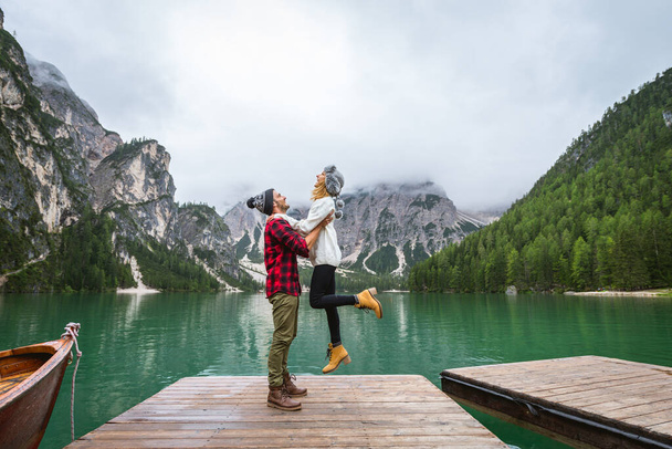 Beautiful couple of young adults visiting an alpine lake at Braies, Italy - Tourists with hiking outfit having fun on vacation during autumn foliage - Concepts about travel, lifestyle and wanderlust - 写真・画像