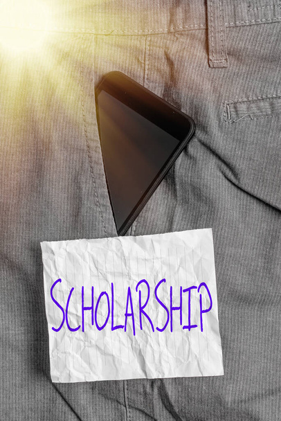 Text sign showing Scholarship. Conceptual photo grant or payment made to support a student s is education Smartphone device inside formal work trousers front pocket near note paper. - Photo, Image