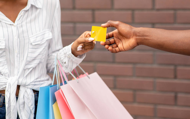 Käuferin mit farbigen Taschen gibt Verkäuferin Kreditkarte - Foto, Bild
