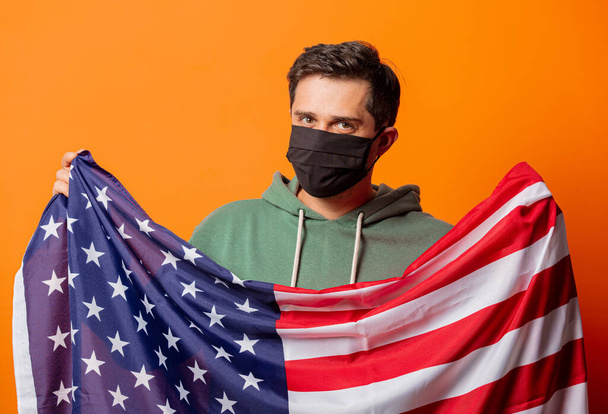 ragazzo in maschera viso e cappuccio verde con bandiera USA su sfondo arancione - Foto, immagini