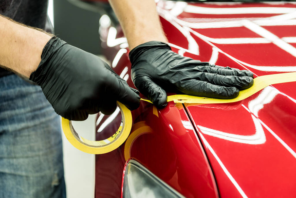 Car service worker applying protective tape on the car details before polishing. - Foto, Bild