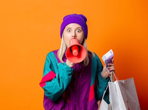 Stile donna in tuta anni '90 con megafono e shopping bag su sfondo arancione - Foto, immagini