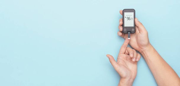 Man using glucometer, checking blood sugar level. Wide image with copy space, blue background. Diabetes concept - Photo, image