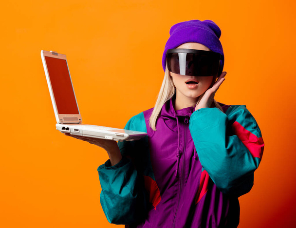 Style woman in 90s tracksuit and VR glasses with notebook on orange background - Valokuva, kuva