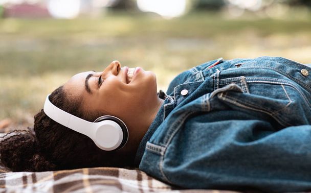 Siyahi kadın müzik dinliyor Ekose üzerinde uzanıyor Park 'ta dinleniyor - Fotoğraf, Görsel