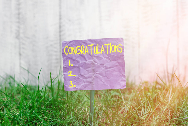 Conceptual hand writing showing Congratulations. Business photo text a congratulatory expression usually used in plural form Plain paper attached to stick and placed in the grassy land. - Photo, Image