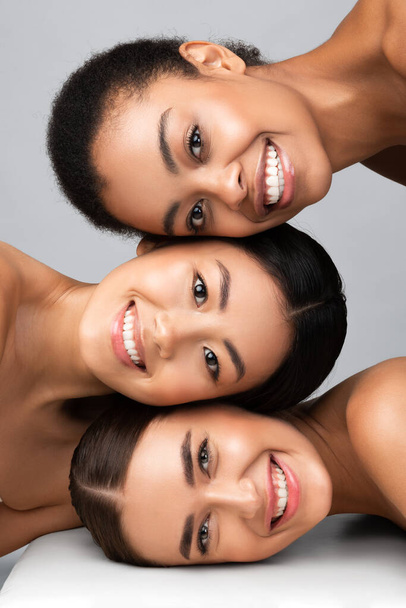 Trzy różne kobiety pozowanie razem uśmiecha się na szarym tle, pionowe - Zdjęcie, obraz