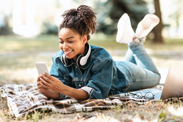 Africaine Millennial Lady en utilisant Smartphone allongé sur plaid dans le parc - Photo, image