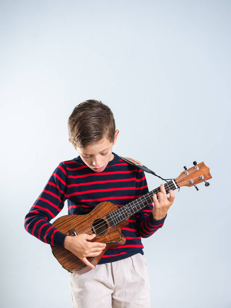7-jähriger Junge spielt Ukelele, isoliert auf grauem Hintergrund - Foto, Bild