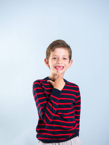 Ritratto di un bambino di 7 anni che indica il suo dente anteriore mancante, isolato su sfondo grigio - Foto, immagini
