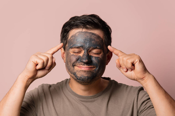 funny guy with a cosmetic mask on his face on pink background - Foto, imagen