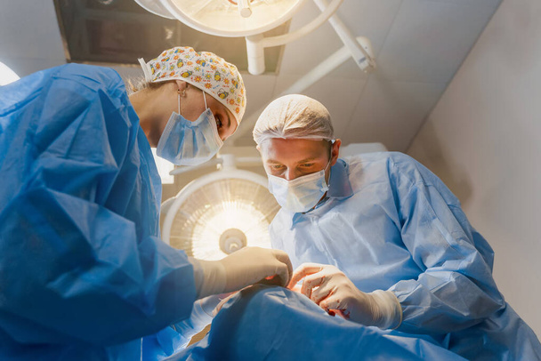 Βλεφαροπλαστική πλαστική χειρουργική επέμβαση για την τροποποίηση της περιοχής των ματιών του προσώπου στην ιατρική κλινική. 2 γιατροί κάνουν πλαστική πλαστική χειρουργική για τη γυναίκα. Χειρουργός ράβει το βλέφαρο - Φωτογραφία, εικόνα