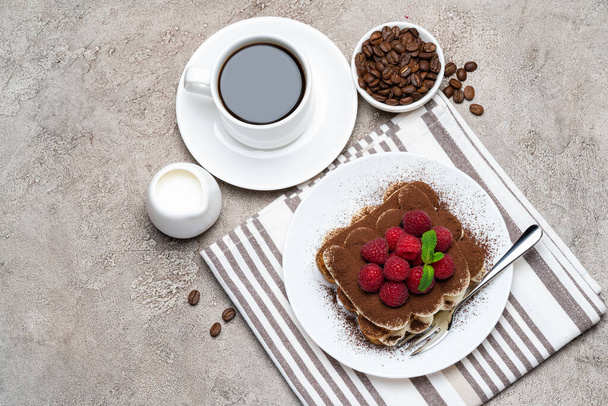 portion of Classic tiramisu dessert with raspberries and cup of coffee and cream or milk on grey concrete background - Zdjęcie, obraz
