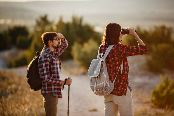 Portrait de jeune couple heureux s'amusant lors de leur voyage de randonnée. Couple de randonneurs caucasiens et asiatiques s'amusant en vacances d'été. Ils observent la nature avec des jumelles. - Photo, image