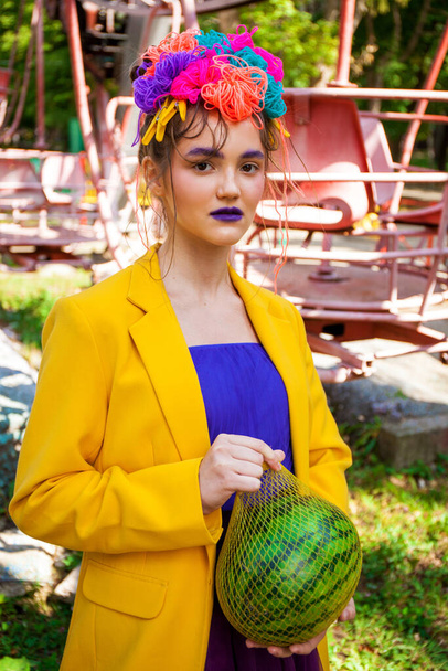Portrét stylového modelu ve žlutém kabátě pózujícího na pozadí zábavního parku  - Fotografie, Obrázek