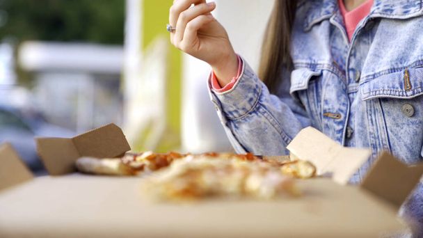 Beautiful woman eating pizza on street. Media. Woman snacking on pizza for lunch outside cafe. Young woman eats pizza on background of busy city - Photo, Image