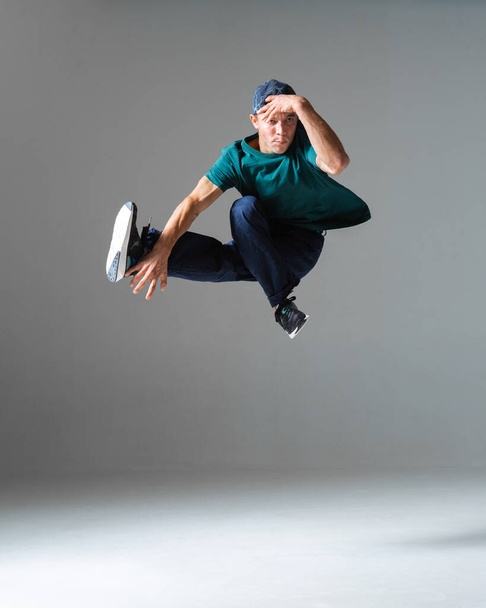 Cool young guy breakdancer jumps in studio isolated on gray background. Dance school poster. Break dance lessons - Fotoğraf, Görsel