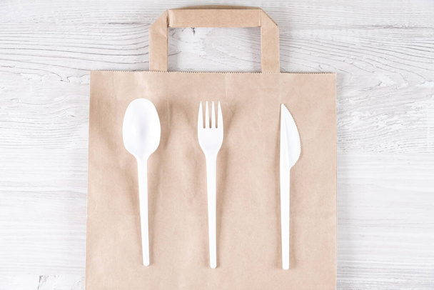 Catering and street fast food plastic fork, spoon, knife on paper bag.Eco-friendly food packaging and cotton eco bags on gray background with copy space. Carering of nature and recycling concept. - Foto, Bild