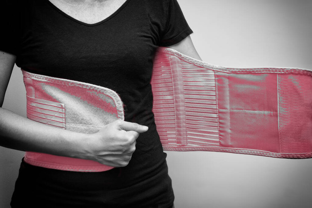 Kobieta w czarnym t-shircie nosząca pas podporowy na ból pleców i kręgosłupa. Czarno-biały ton. Koncepcja opieki medycznej - Zdjęcie, obraz