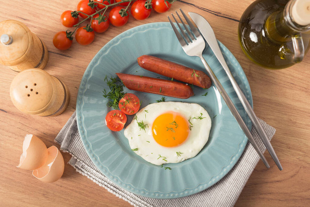 Délicieux petit déjeuner composé d'œufs frits, de saucisses de porc et de tomates fraîches sur une table de cuisine. - Photo, image
