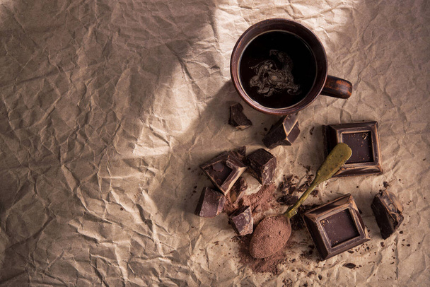 Grandes pedaços de chocolate escuro, cacau em pó e xícara de café em papel artesanal. vista superior. espaço de cópia - Foto, Imagem