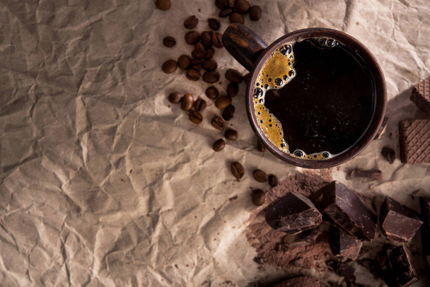 Große Stücke dunkler Schokolade, Kakaopulver und Kaffeetasse auf Bastelpapier. Ansicht von oben. Kopierraum - Foto, Bild