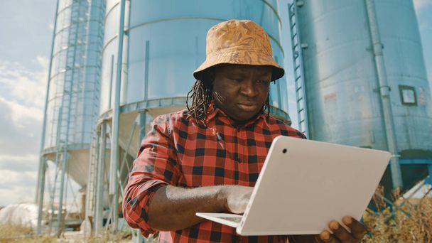 Afrikkalainen viljelijä, joka käyttää kannettavaa tietokonetta siilon varastointijärjestelmän edessä - Valokuva, kuva