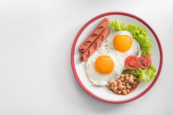 Αγγλικό πρωινό με τηγανητό αυγό, φασόλια, ντομάτες, λουκάνικα, φρέσκα φύλλα μαρουλιού. Άνω όψη. - Φωτογραφία, εικόνα