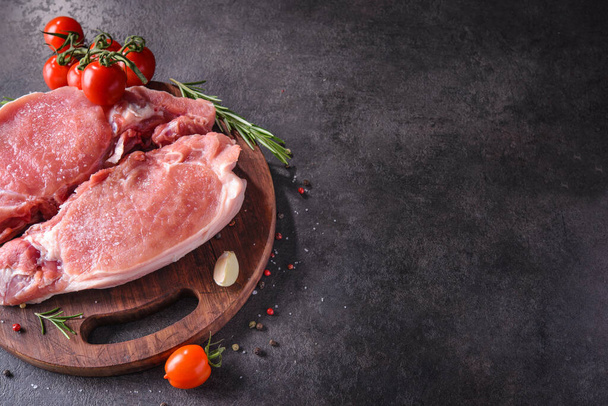 Steak de porc cru sur une planche en bois avec des épices et des ingrédients pour cuisiner. Place pour le texte. - Photo, image
