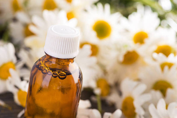 Botella de vidrio con aceite esencial de manzanilla con flores en una mesa de madera. concepto orgánico cosmético y médico. - Foto, imagen