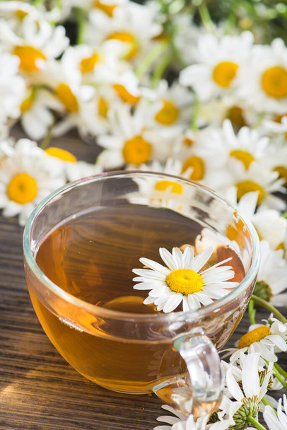 Γυάλινο κύπελλο με τσάι βοτάνων με λουλούδια χαμομηλιού σε ξύλινο φόντο. Υγιεινό ποτό. - Φωτογραφία, εικόνα