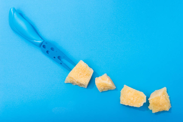 Tasty parmesan yellow cheese pieces on a blue background. Color and minimal concept. - Photo, Image